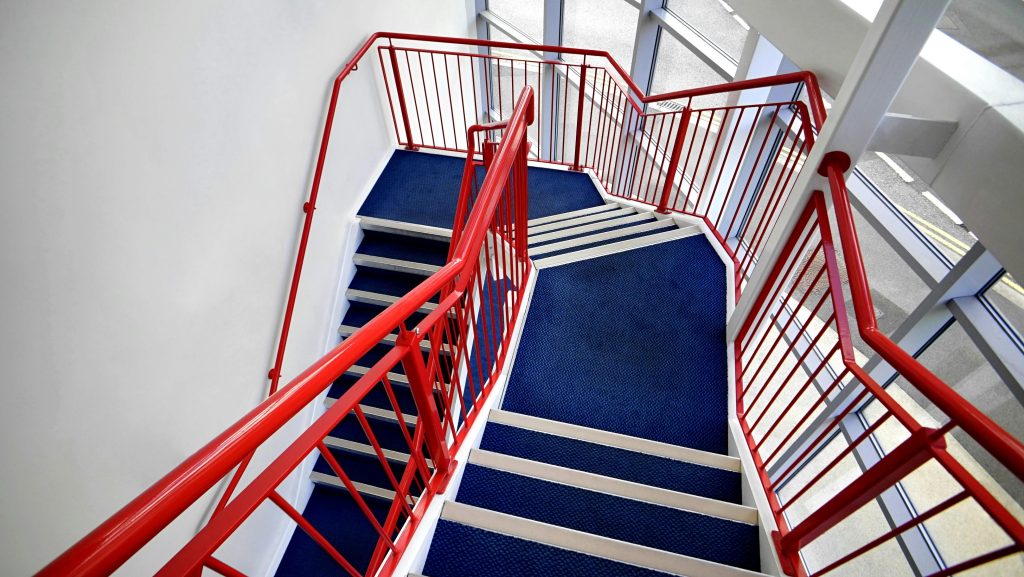 Interior staircase with red railings and blue carpet, showcasing modern architectural design.
